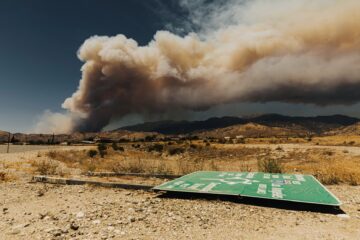 barren landscape with broken road sign and plume of smoke